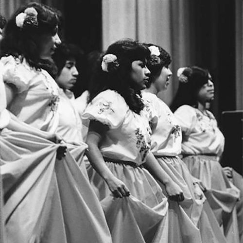 Several people in dresses are standing and holding up their skirts while dancing. Caption reads: 'A dance group, the Los Bailarimos Folkloricos de Waukesha, performed Sunday at a church festival at the Waukesha County Exposition Center.'            Varias personas, usando vestidos, están de pie y sosteniendo sus faldas mientras bailan. El título dice: 'Un grupo de baile, Los Bailarimos Folkloricos de Waukesha, actuó el domingo en un festival de la iglesia en el Centro de Exposiciones del Condado de Waukesha.                        